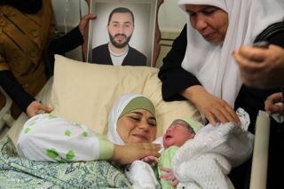 Dallal melihat bayinya yang baru lahir dengan foto suaminya yang sedang dipenjara Israel, Amer al-Zein, 13 Agustus 2013. (AFP, Jaafar Ashtiyeh)
