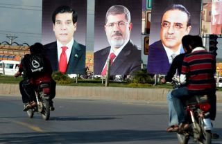 Seorang pengendara motor di Pakistan melintasi bilboard yang menampilkan potret Presiden Mesir Muhammad Mursi (tengah), Presiden Pakistan Asif Ali Zardari (kanan), dan Perdana Menteri Raja Pervez Ashraf (kiri) di sebuah jalan di Islamabad pada tanggal 17 Maret 2013. (AFP PHOTO / Aamir Qureshi)
