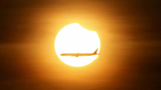 Sebuah pesawat melintasi matahari yang mulai 'disentuh' bulan, 9 Maret 2016. (Reuters/Edgar Su)