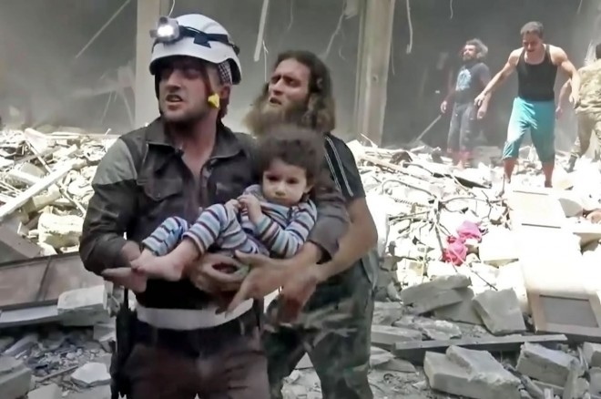 Foto cuplikan dari video yang dipublikasikan secara online oleh UGC, seorang pekerja Pertahanan Sipil setempat menggendong seorang anak korban serangan udara yang menimpa Aleppo, Suriah, Kamis (28/5/2016). (Validated UGC / Associated Press)